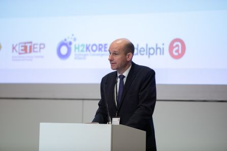 Close up of speaker presenting, Logos of KETEP, H2KOREA and adelphi in the background visible