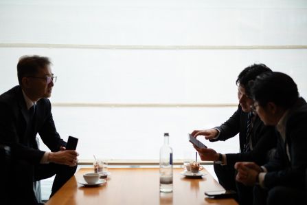 Three people sitting and chatting over coffee, one of them showing something to another one