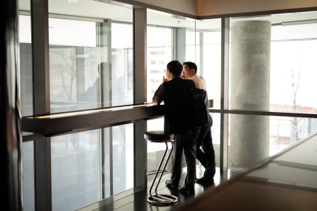 Two people standing on a high table on a window, chatting and looking outside